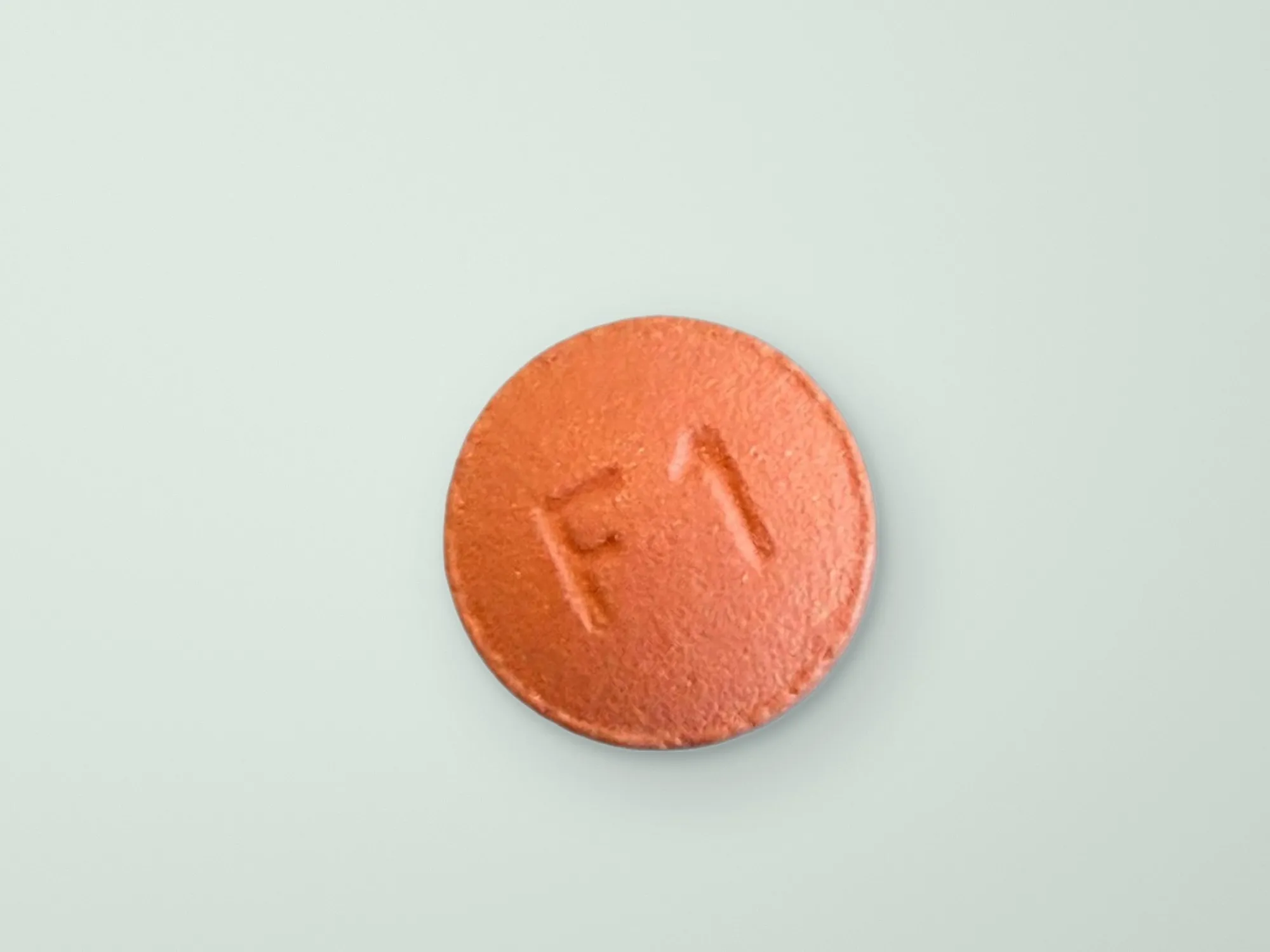 An orange tablet on a light, sage green background